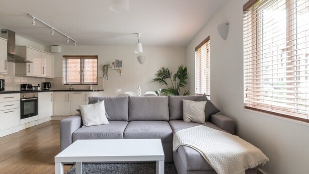 Ein modernes Wohnzimmer mit einem grauen Sofa, einem weißen Couchtisch und einer Küche im Hintergrund.