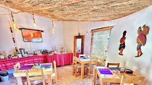 Ein Essbereich mit Holztischen und -stühlen, einem an der Wand montierten Fernseher und einem Buffet mit verschiedenen Speisen.