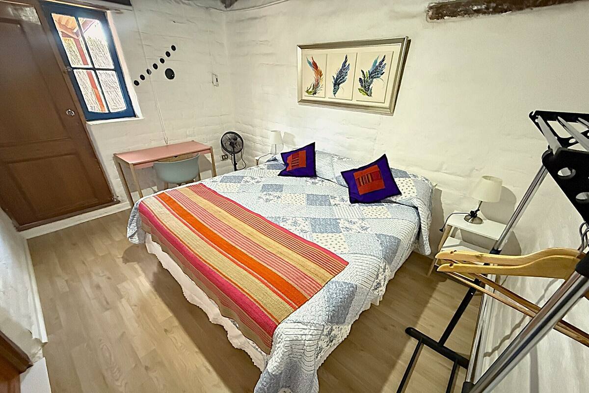 A bedroom with a bed, a wooden floor, a desk, a chair, a window, and a door.