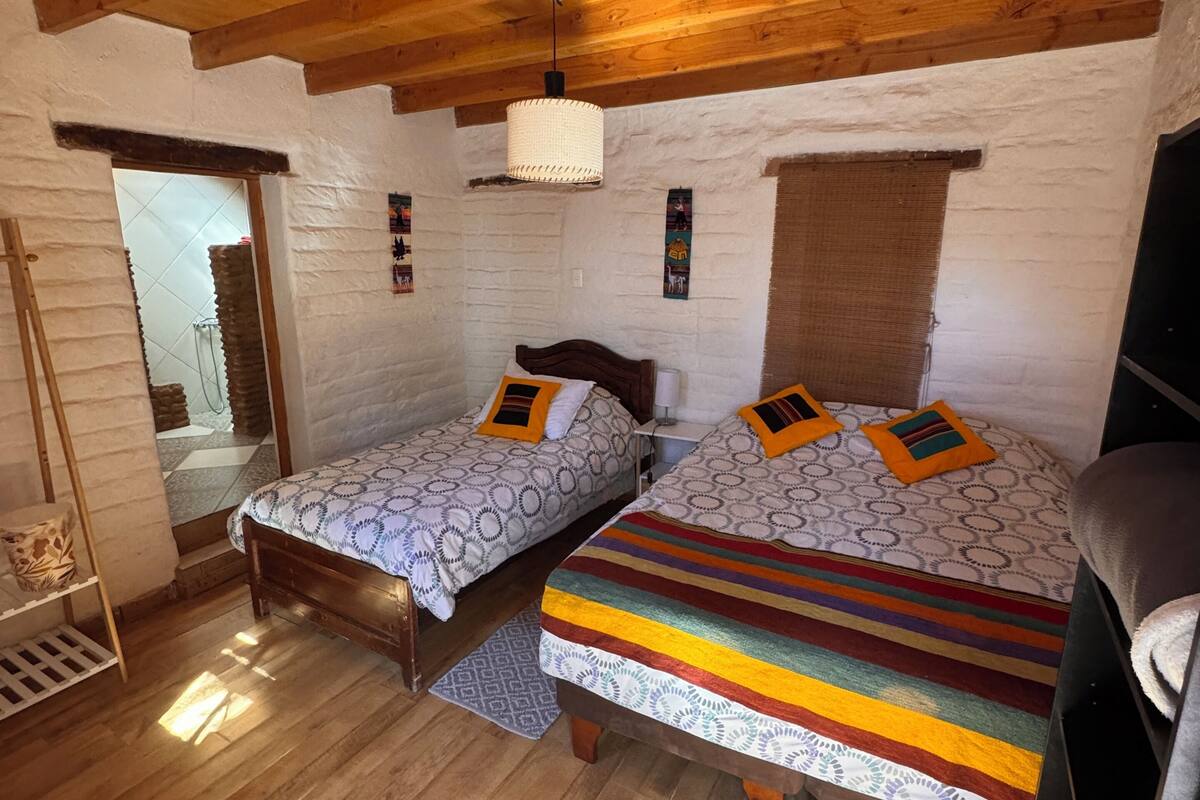 A cozy room with two wooden beds, a wooden ceiling, and a white brick wall.