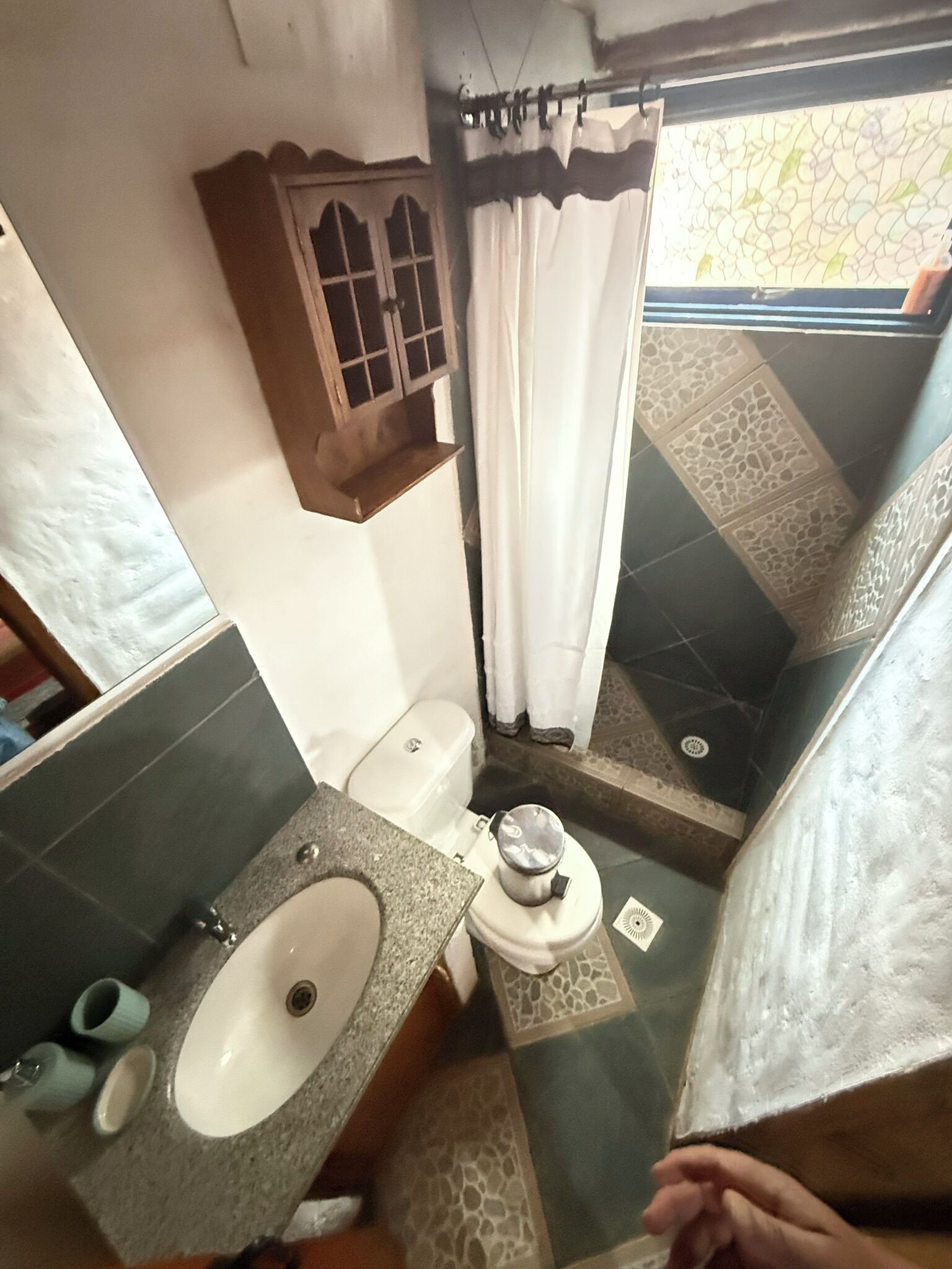 A compact bathroom with a sink, toilet, and a small window with curtains.
