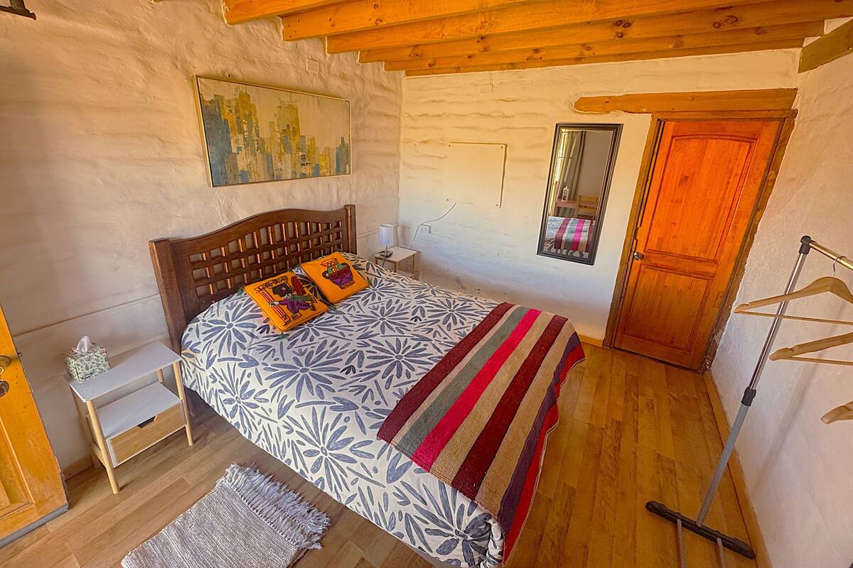 A bedroom with a wooden bed, a nightstand, a bedside table, a mirror, a wooden door, and a hanging clothes rack.