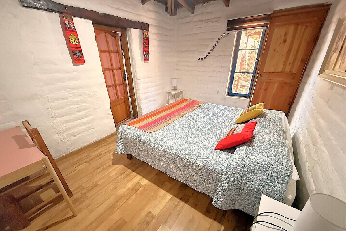A bedroom with a bed, a chair, a desk, and a window.