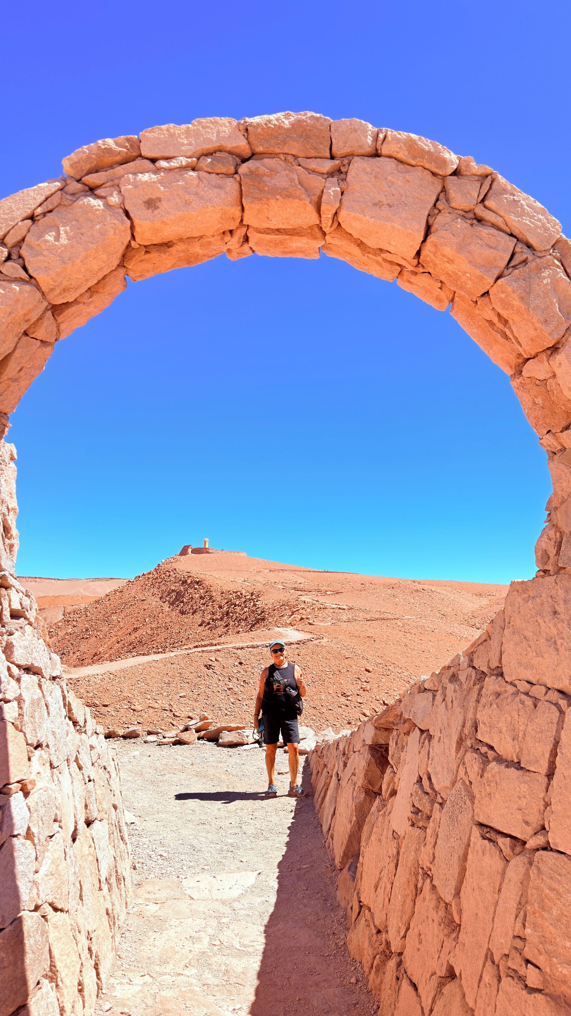 A person standing in a stone archway with a clear blue sky in the background.