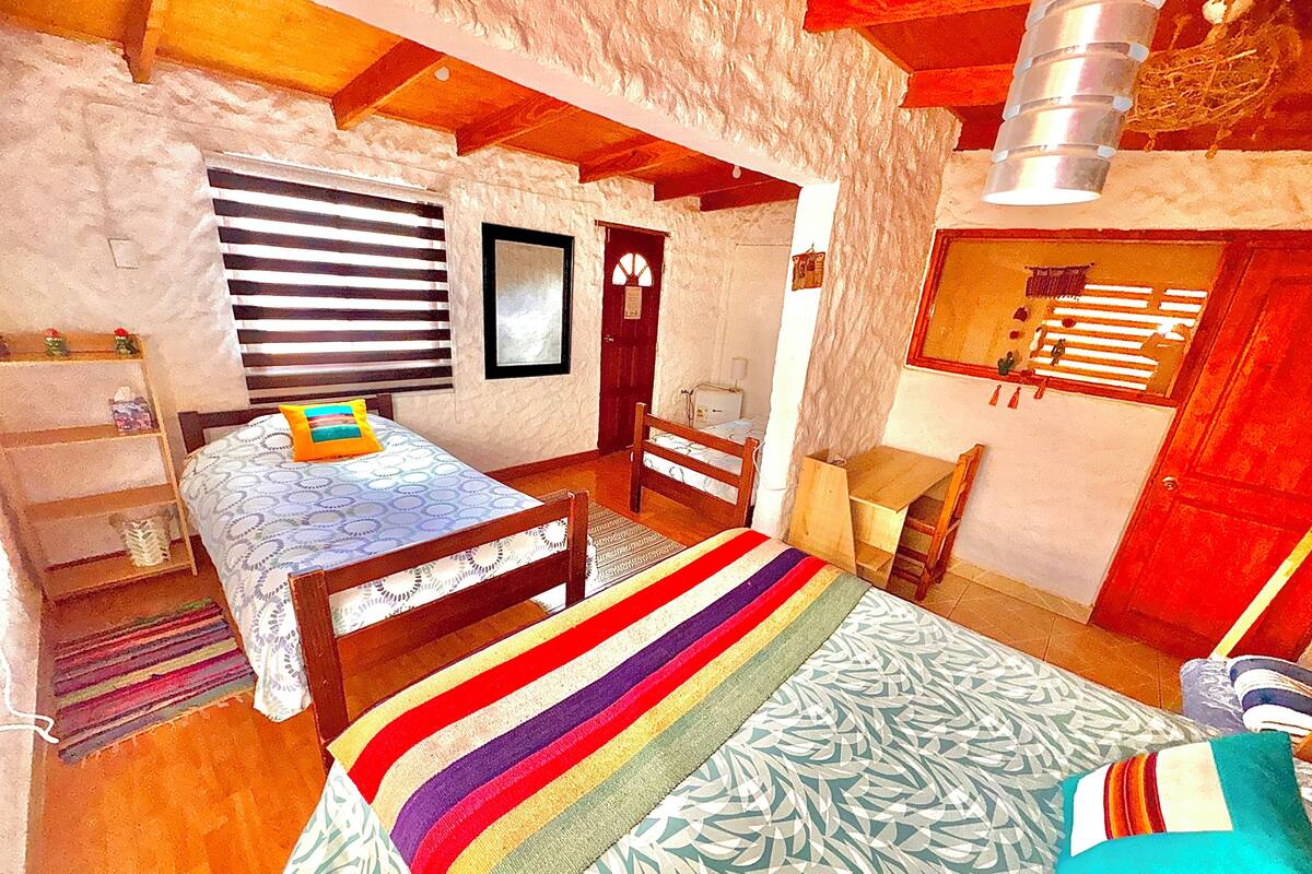 A bedroom with a bed, a desk, a chair, a wardrobe, and a window with blinds.