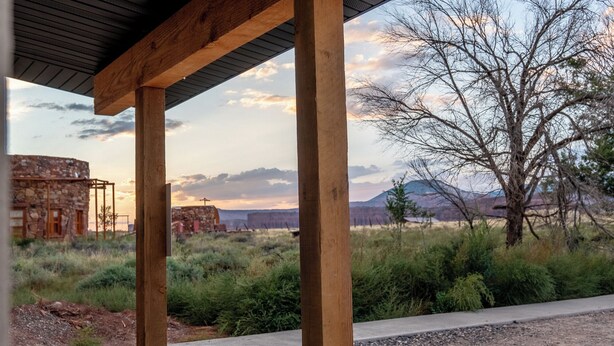 Eine hölzerne Pergola mit Blick auf ein Steinhaus und einen Baum in einer natürlichen Landschaft.