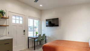 Ein Zimmer mit einem Bett, einem Schreibtisch mit Stuhl, einem an der Wand montierten Fernseher und einer Tür mit Fenster.