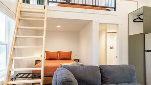 Ein Schlafzimmer im Loft-Stil mit einem Etagenbett, einem grauen Sofa und einer Holzleiter.