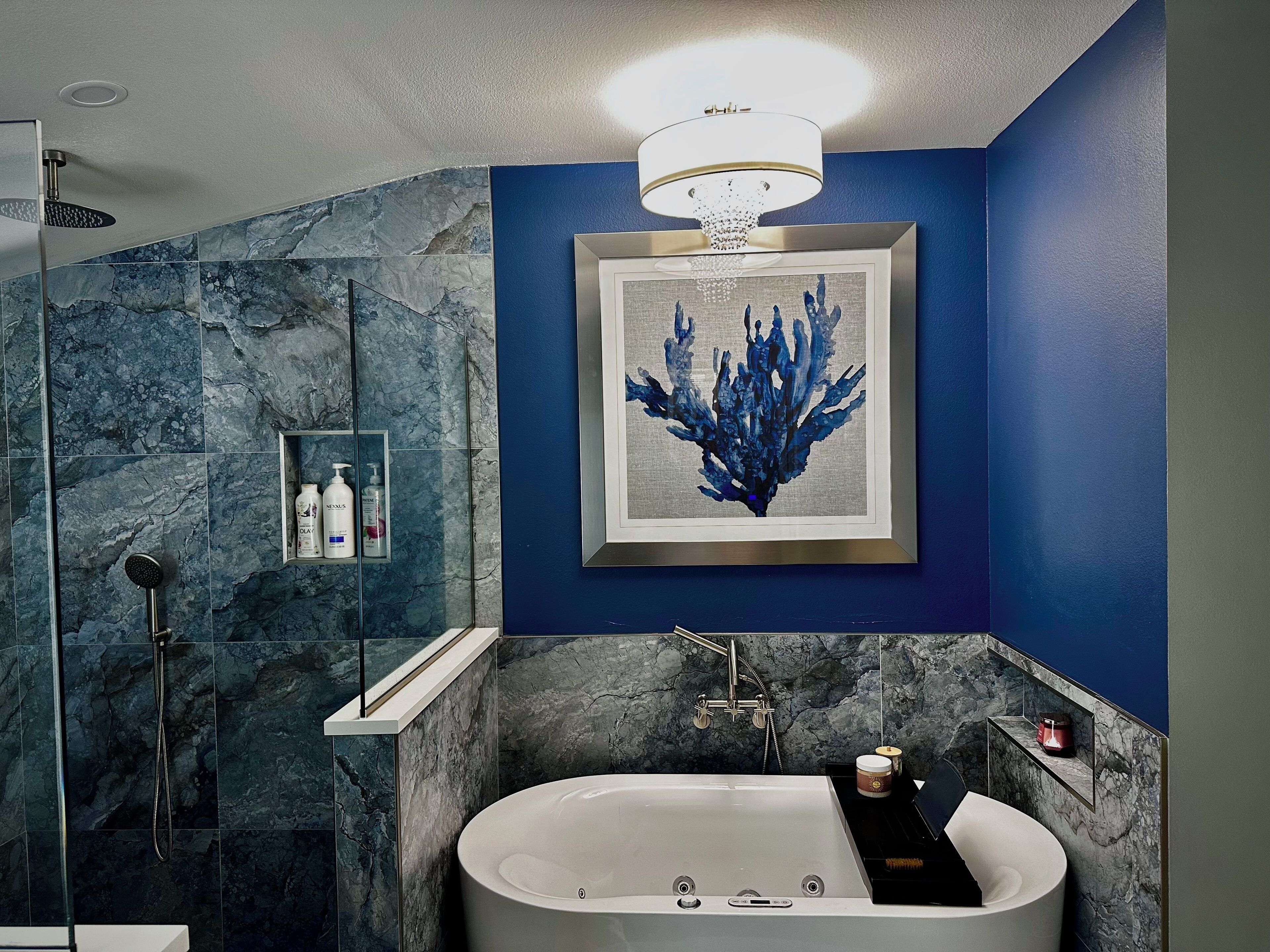 Une salle de bain moderne avec une baignoire, une douche et une œuvre d’art encadrée représentant des coraux bleus, accrochée au mur.