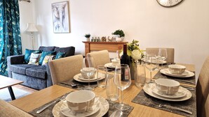 A dining area with a wooden table set for a meal, a sofa, a clock, and a painting on the wall.