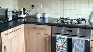 A modern kitchen with wooden cabinets, a gas stove, a toaster, and a kettle.