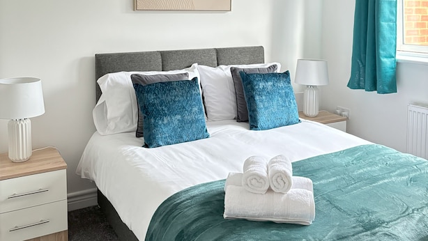 A neatly arranged bedroom with a bed, bedside tables, a hanging light fixture, a window with curtains, and a wall-mounted artwork.