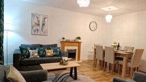 A living room with a sofa, chairs, a dining table, a fireplace, and a clock on the wall.