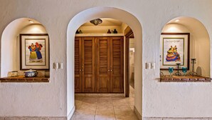 A hallway with arched doorways, wooden doors, and framed artwork on the walls.