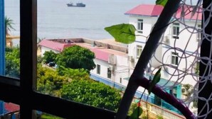 A view from a window overlooking a coastal area with buildings and a ship in the distance.