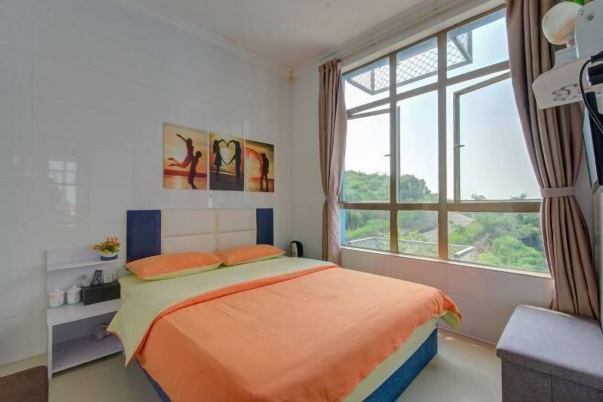 Ein Schlafzimmer mit Bett, Nachttisch, einem Fenster mit Vorhängen und einem Kunstwerk an der Wand.