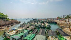 A harbor with numerous boats docked, a pier with a covered walkway, and rocky shores.