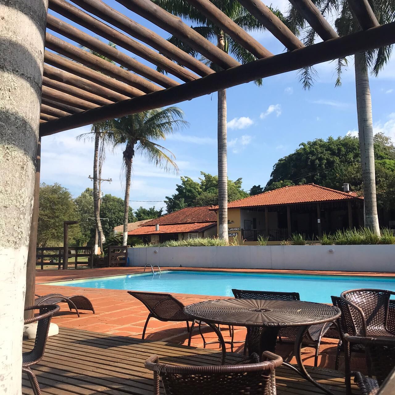 Area piscina con un solarium in legno, mobili in vimini e un edificio sullo sfondo con un tetto in tegole rosse.