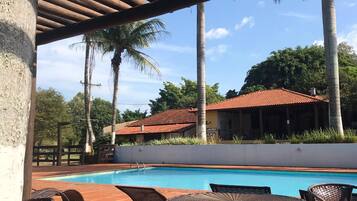 Area piscina con un solarium in legno, mobili in vimini e un edificio sullo sfondo con un tetto in tegole rosse.
