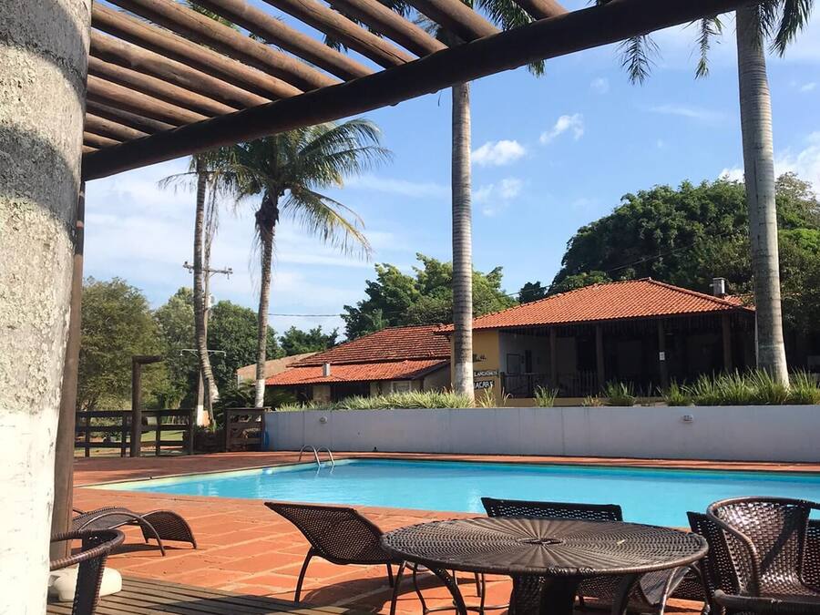 A pool area with a wooden deck, wicker furniture, and a building with a red-tiled roof in the background.