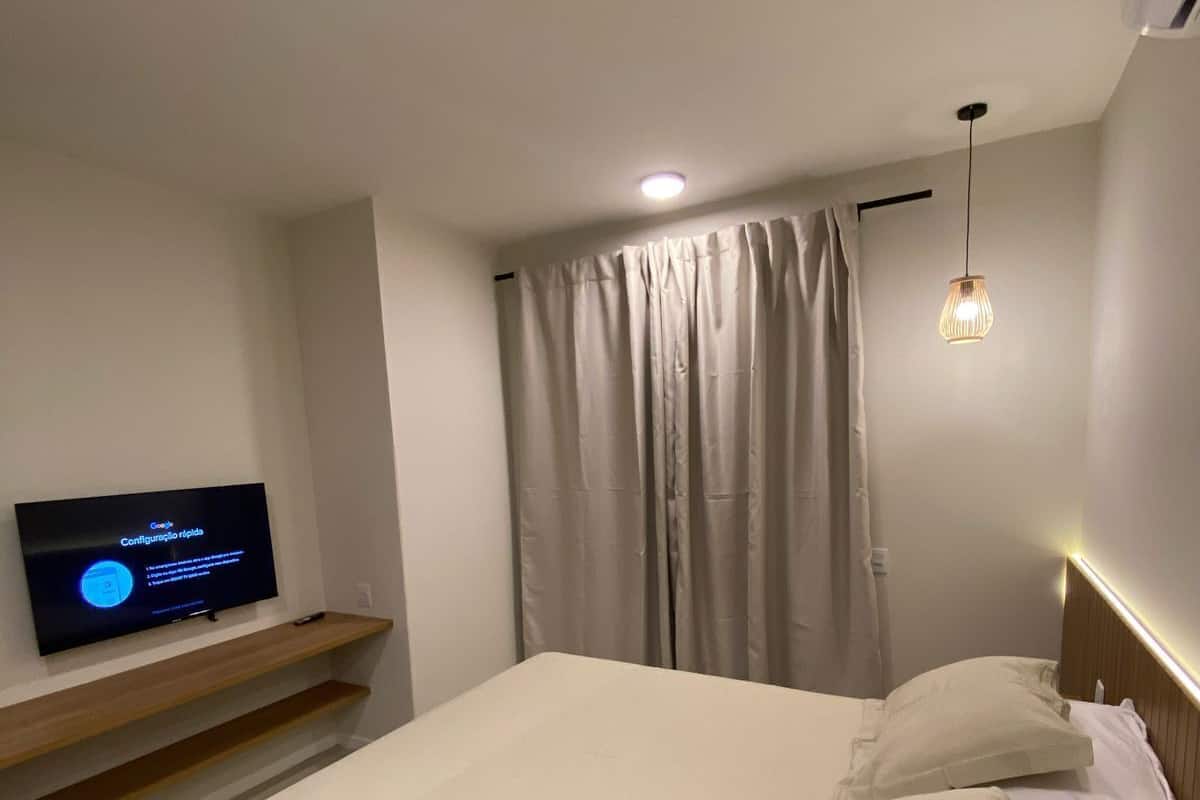 Un dormitorio ordenado con una cama, un televisor en un estante y una lámpara colgante.