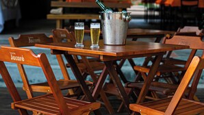 A wooden table with a metal bucket and two glasses of beer, surrounded by wooden chairs. - Vila Jacaré (Brotas)
