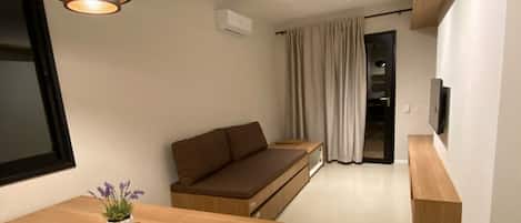 A modern living room with a wooden coffee table, a brown sofa, a hanging light fixture, and a television mounted on the wall.