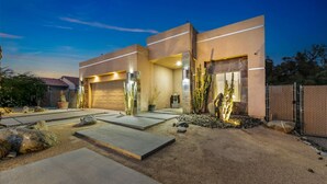 A modern two-story house with a garage, a landscaped driveway, and a well-maintained garden with rocks and plants. - Gorgeous Tranquil Desert Retreat (Desert Hot Springs)