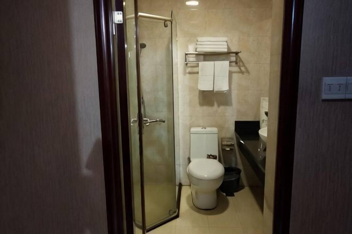 A bathroom with a glass shower enclosure, a toilet, a sink, and a towel rack with towels.