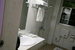 Een badkamer met een wastafel, spiegel, handdoekrek, douche en een raam.
