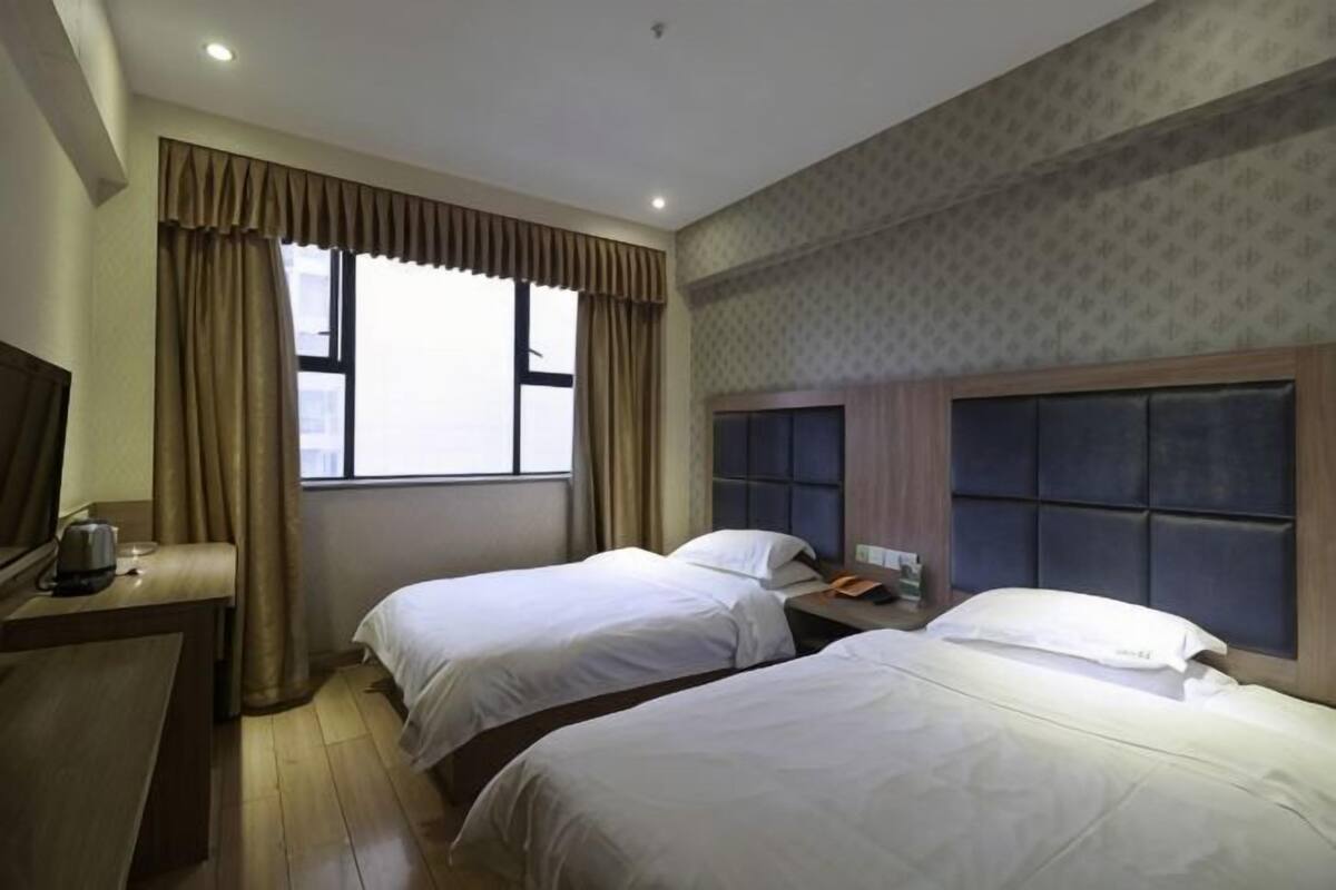 A hotel room with two beds, a desk, a chair, a TV, and a window with curtains.