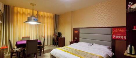 A hotel room with a bed, a desk, and a chair. There is a nightstand with a lamp and a red sign on the wall.