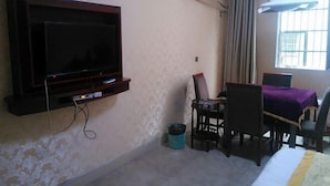 Una habitación con una televisión instalada en la pared, una mesa de comedor con sillas, una ventana con cortinas y un aire acondicionado.