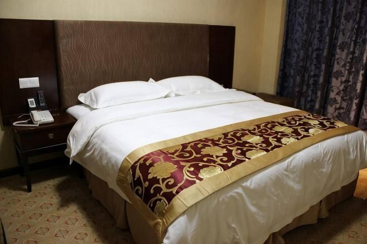 A hotel room with a large bed, a wooden headboard, a bedside table with a phone, and a patterned carpet.