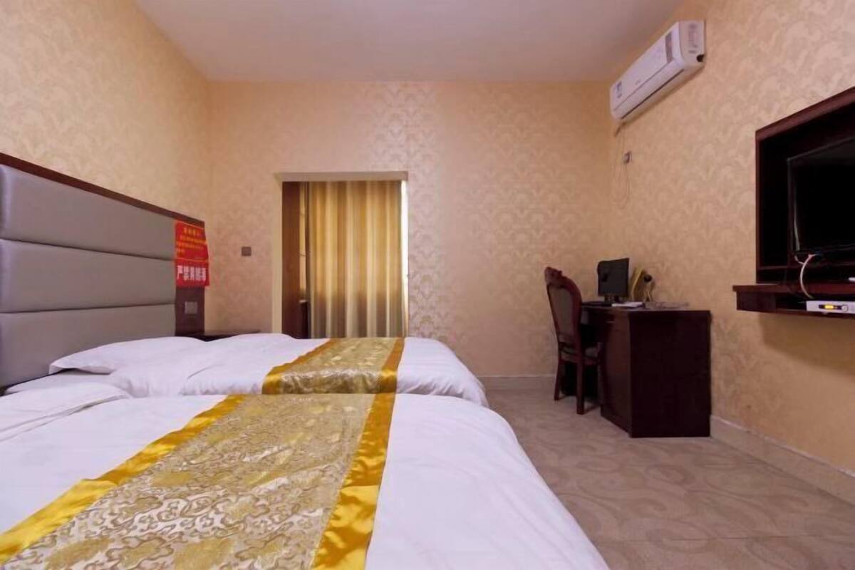 A hotel room with two beds, a desk with a chair, a television, and an air conditioning unit.