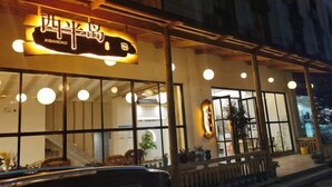 Un restaurante con un letrero que dice "XIBANDAO" y una entrada visible con amplias ventanas y una banca en el exterior.
