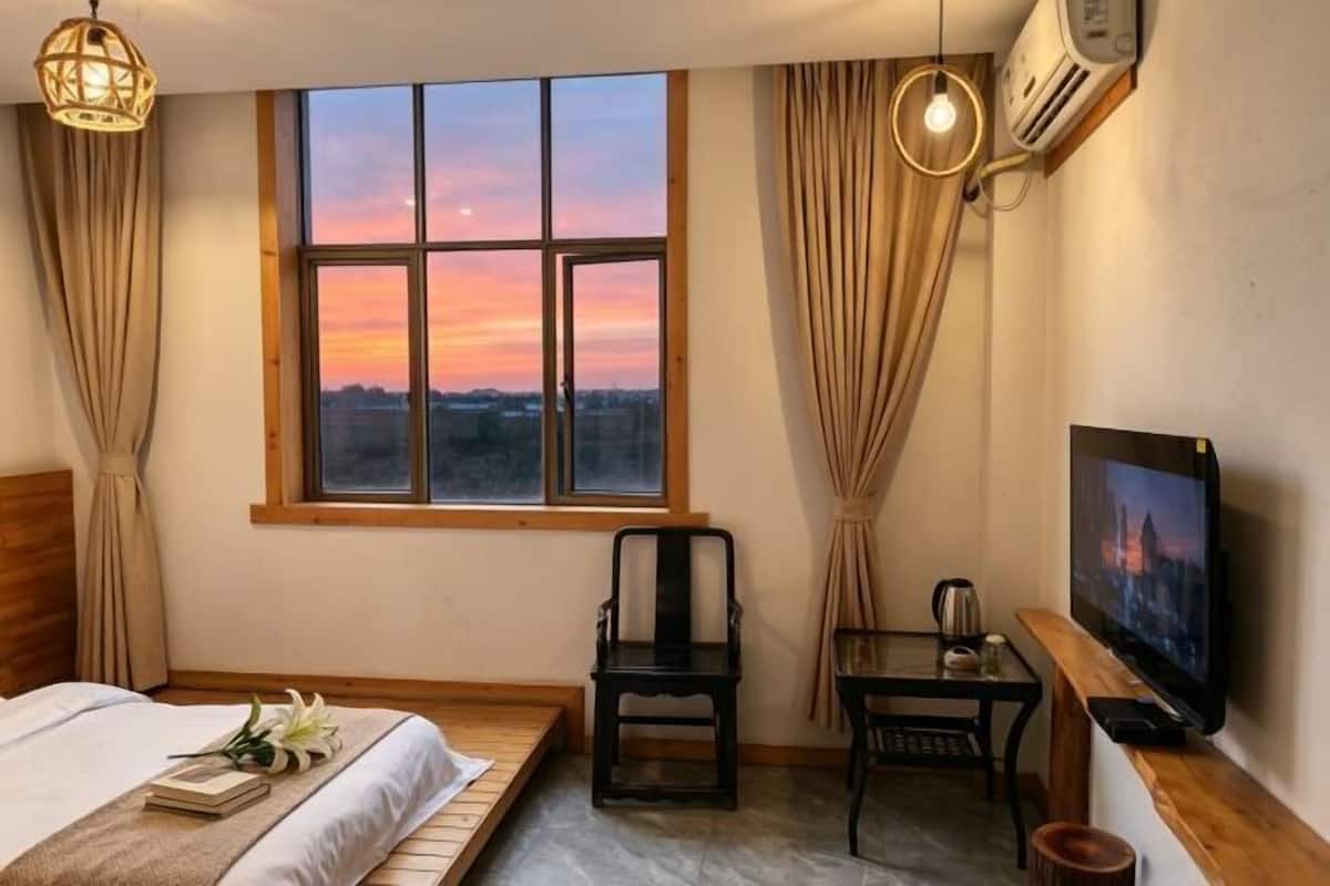 Une chambre d’hôtel avec un lit, une chaise, une table, un téléviseur et une fenêtre donnant sur la ville.