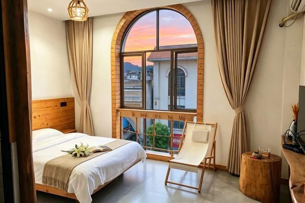 Une chambre avec une grande fenêtre en arc de cercle, un lit, une chaise et une petite table.