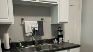 A kitchen with white cabinets, a granite countertop, a stainless steel sink, and a coffee maker.