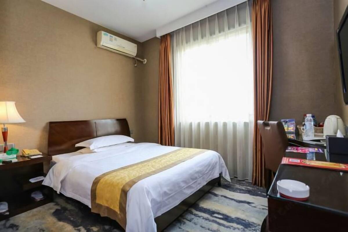Hotellihuone, jossa on sänky, työpöytä, tuoli, lamppu, televisio ja ikkuna, jossa on verhot.