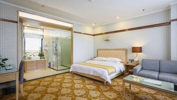 Habitación de hotel con cama, sofá, escritorio y baño con ducha de vidrio.