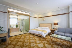 Habitación de hotel con cama, sofá, escritorio y baño con ducha de vidrio.