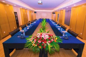 Un salón de conferencias con una larga mesa, sillas y un centro de mesa floral.