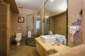 Un baño con cabina de ducha de vidrio, un lavabo blanco y un secador de pelo fijado en la pared.