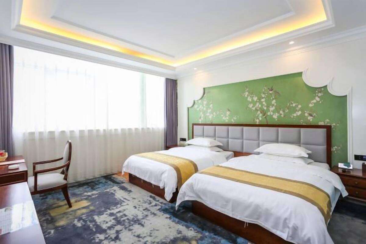 Hotellihuone, jossa on kaksi sänkyä, työpöytä ja tuoli.