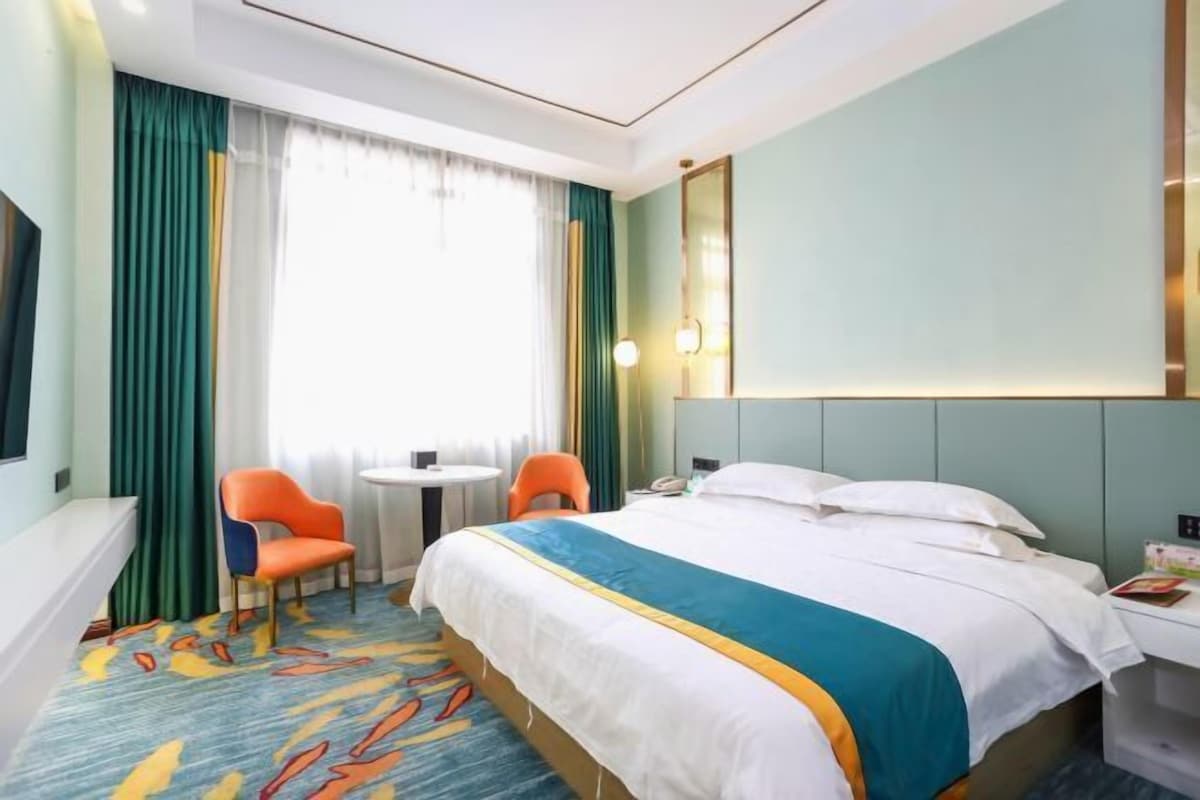A hotel room with a bed, a chair, a small table, and a window with curtains.
