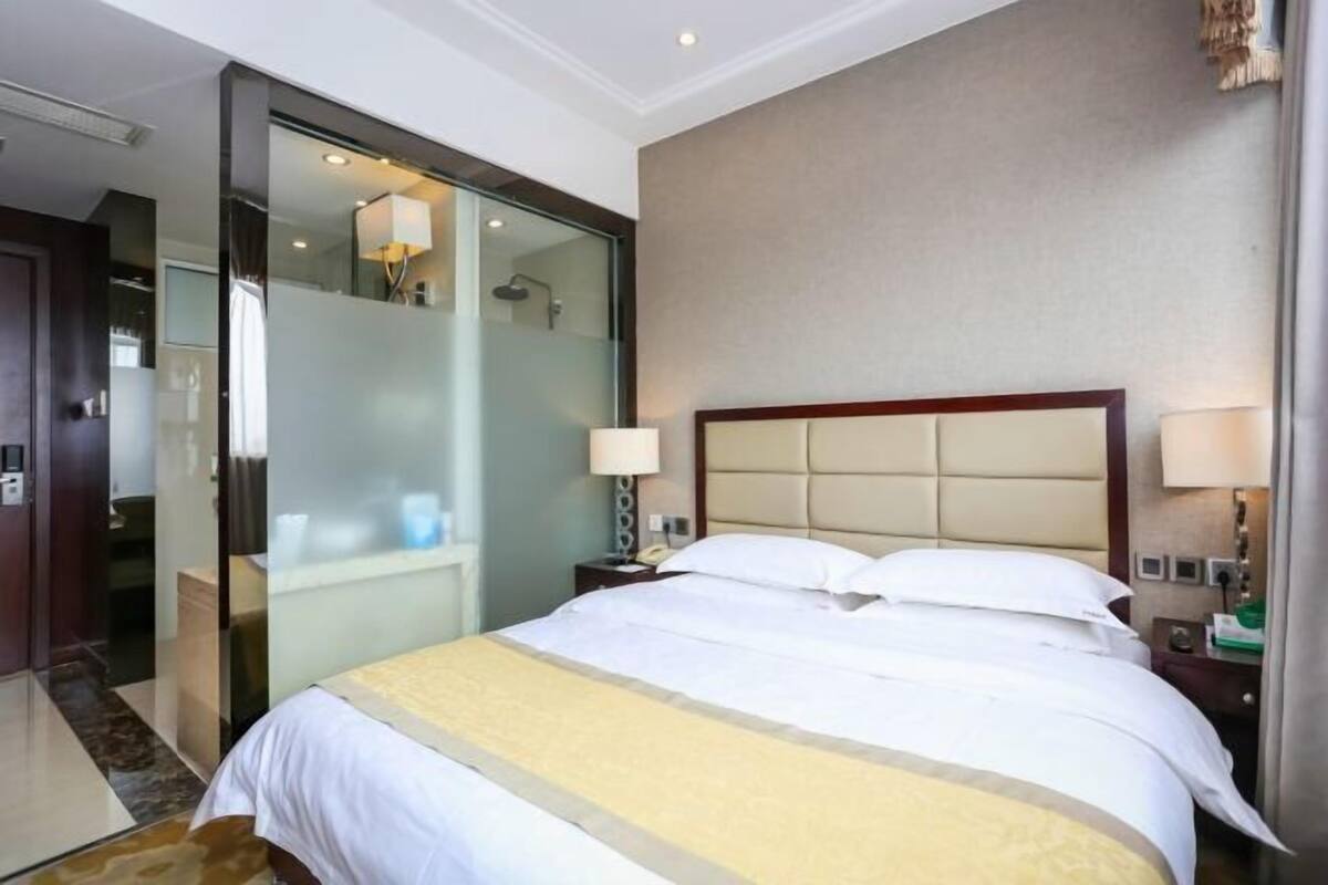 Hotellihuone, jossa on suuri sänky, lasiseinäinen suihkukaappi ja puinen pääty.