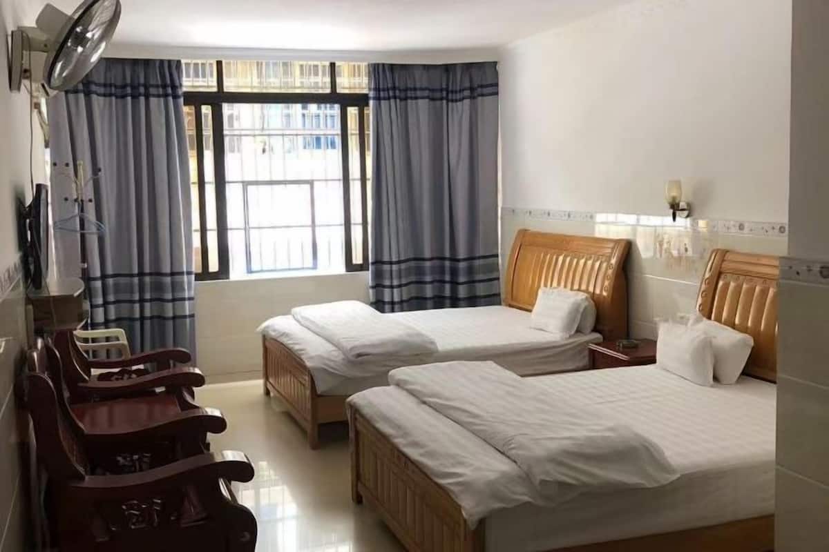 Habitación de hotel con dos camas, cabecera de madera, mesita de noche, una silla y una ventana con cortinas.