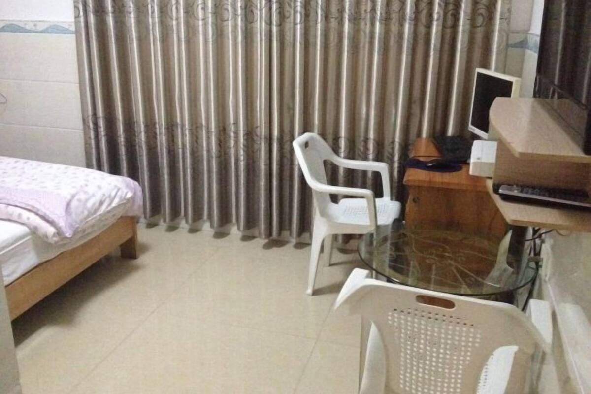 Un dormitorio con una cama, un escritorio con computadora, una silla y una mesa de vidrio.