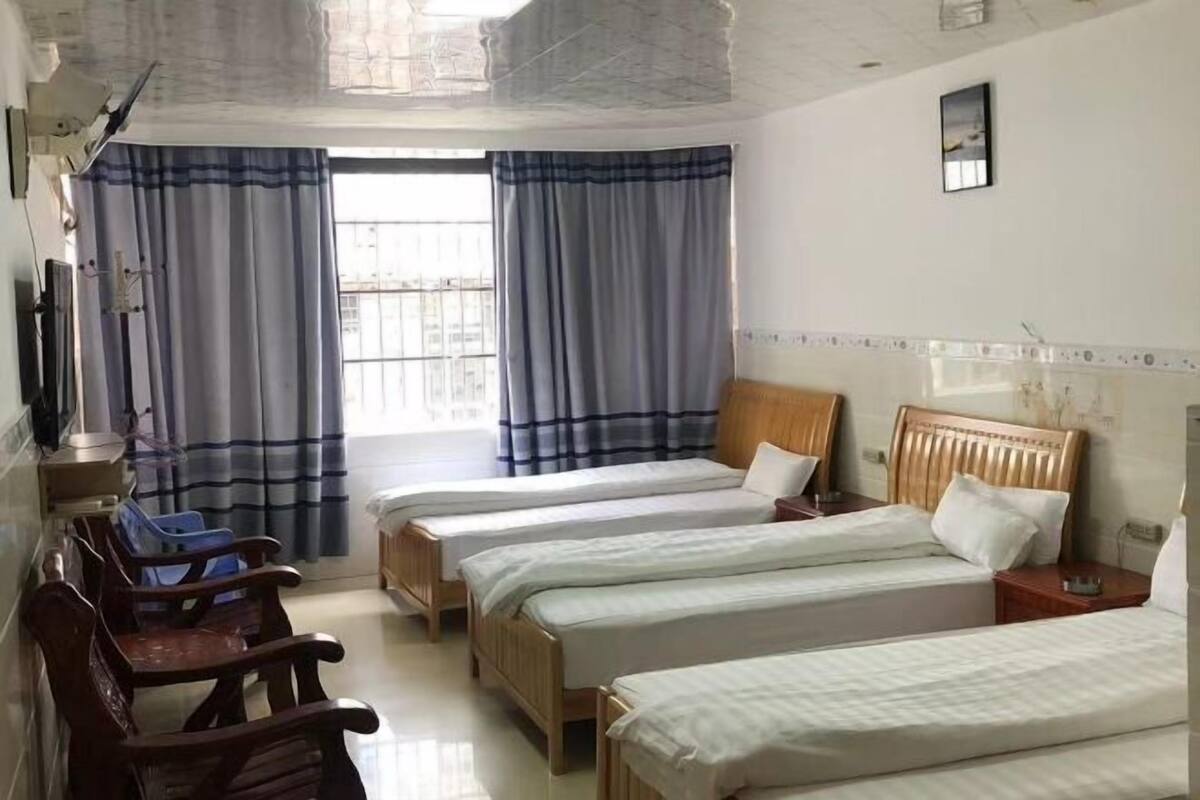 Habitación de hotel con tres camas individuales, cabeceros de madera, un escritorio con silla y una ventana con cortinas.